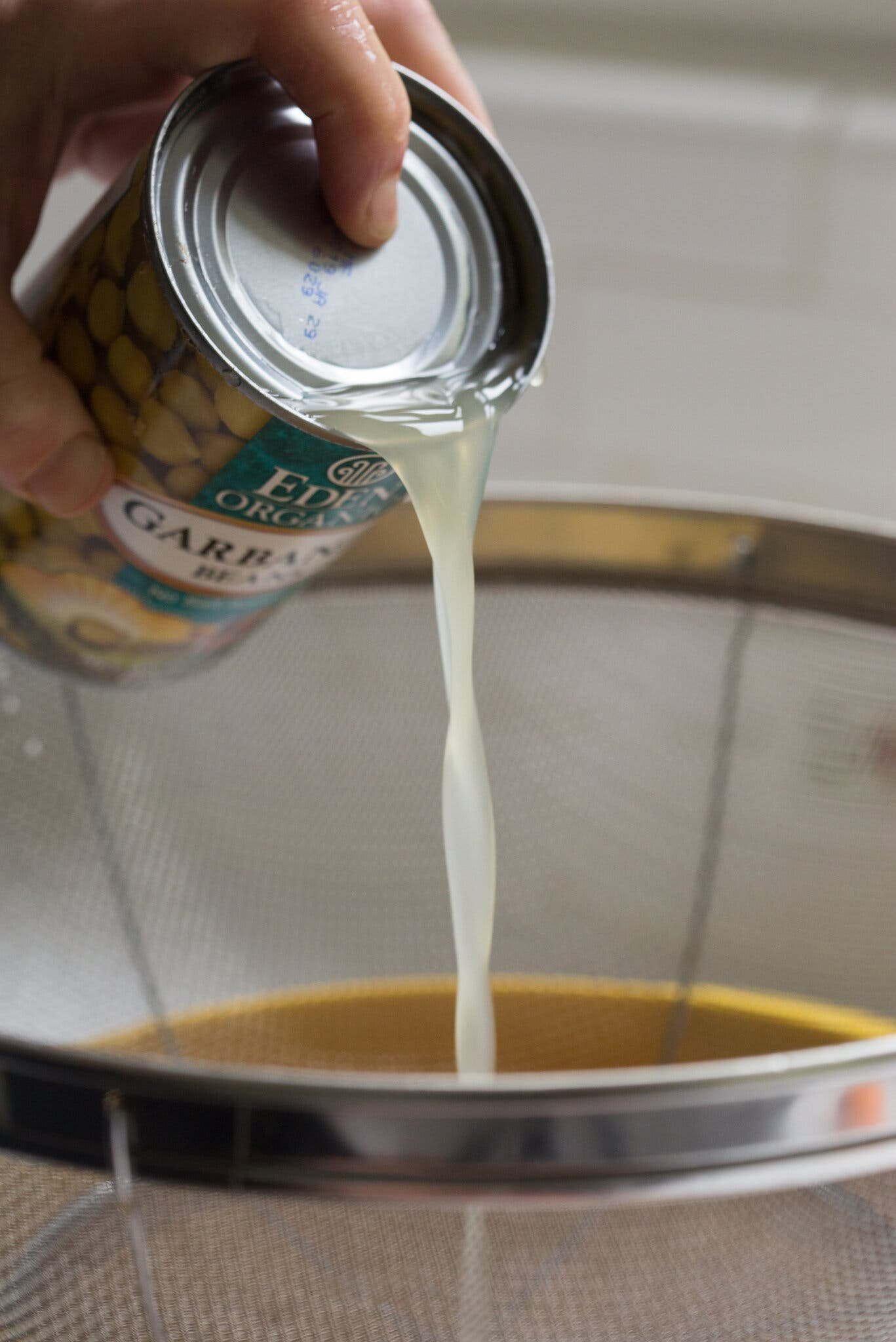 A side image of a hand pouring the liquid from a can of chickpeas into a strainer.